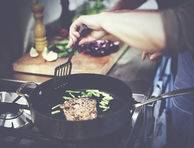a chef is stirring in a pan, which contains a steak and some greens